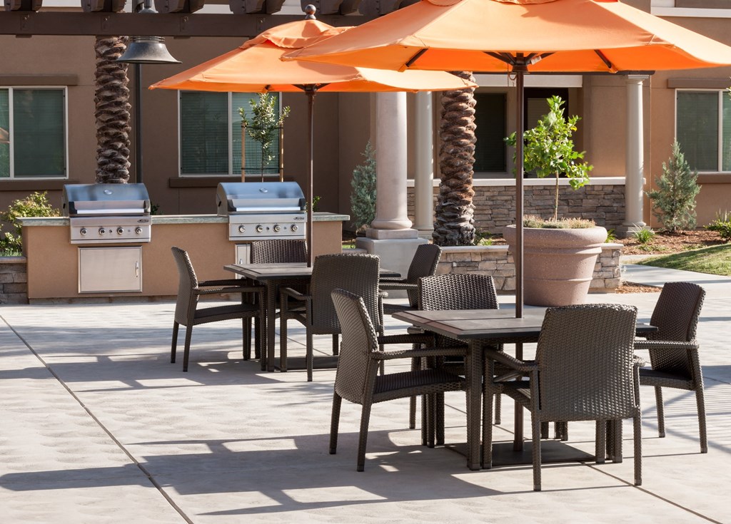 a group of tables with orange umbrellas on a patio with barbeques