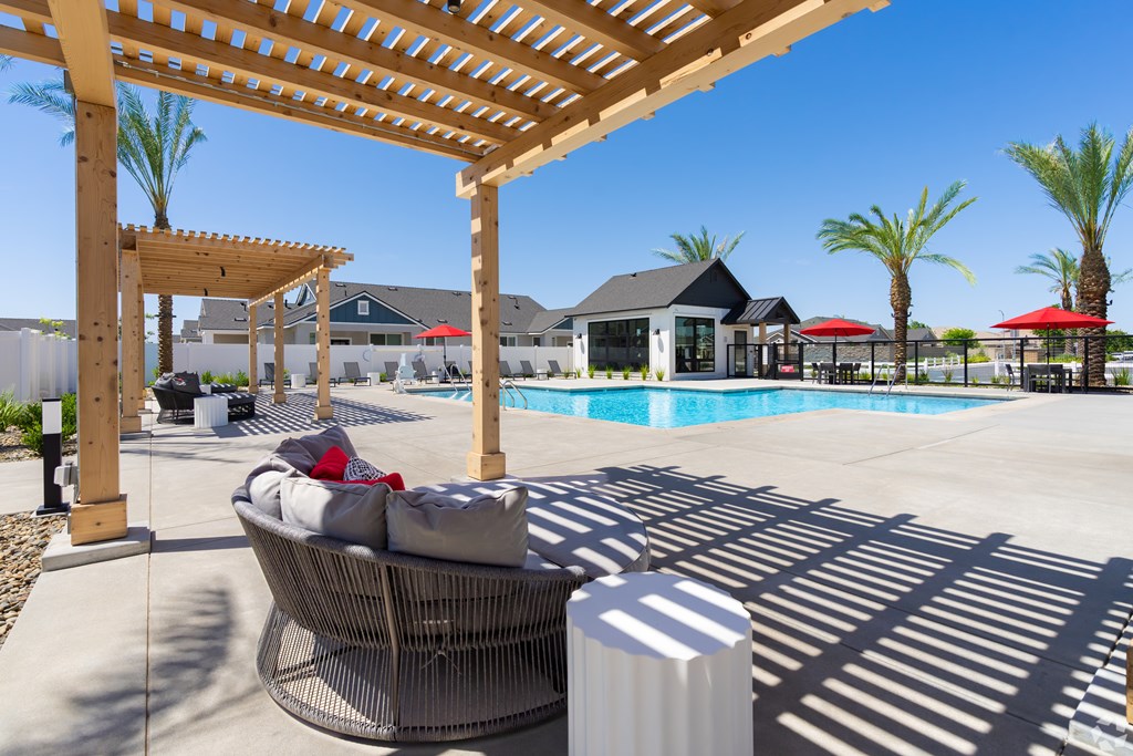 A patio with a wicker chair and a white pillow is under a wooden pergola.