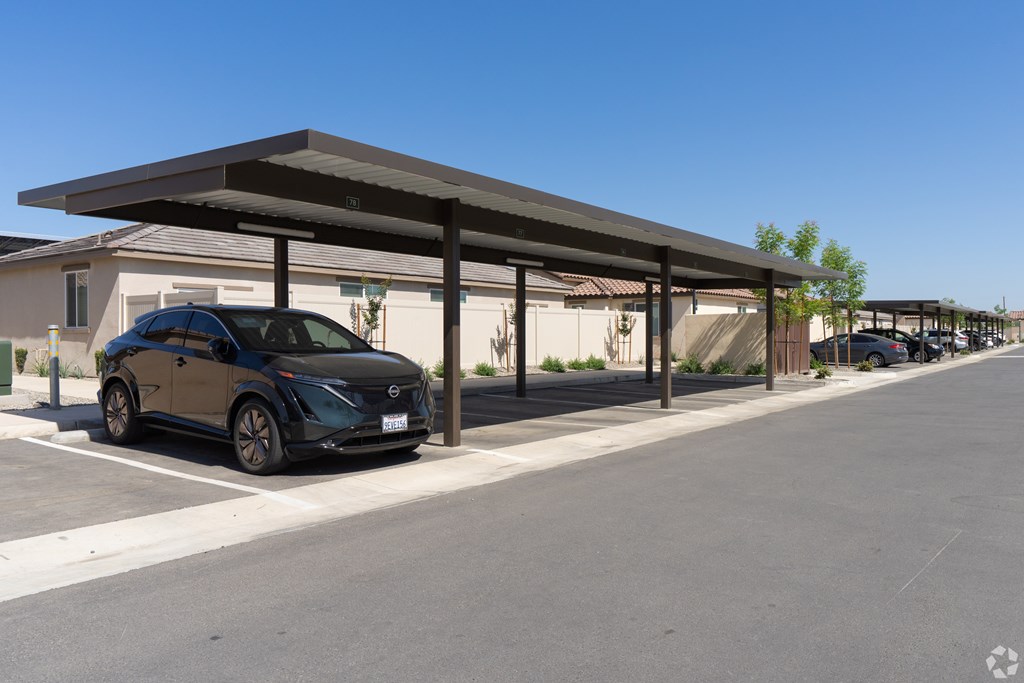 A black car is parked under a covered parking structure.
