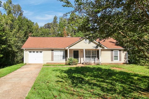 A house with a red roof and a garage door is surrounded by greenery.