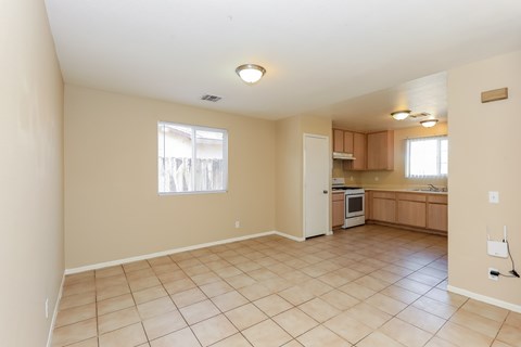 A spacious room with beige walls and tile flooring, featuring a kitchen area with wooden cabinets and appliances.