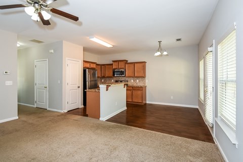 A living room with a ceiling fan and a kitchenette.