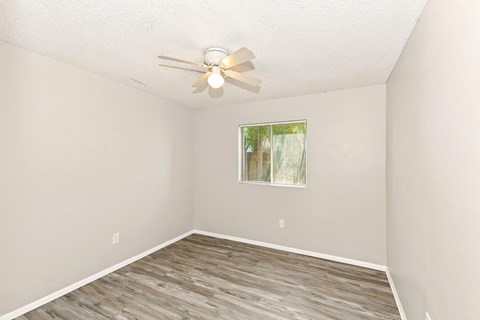 A room with a ceiling fan and a window with a view of trees.