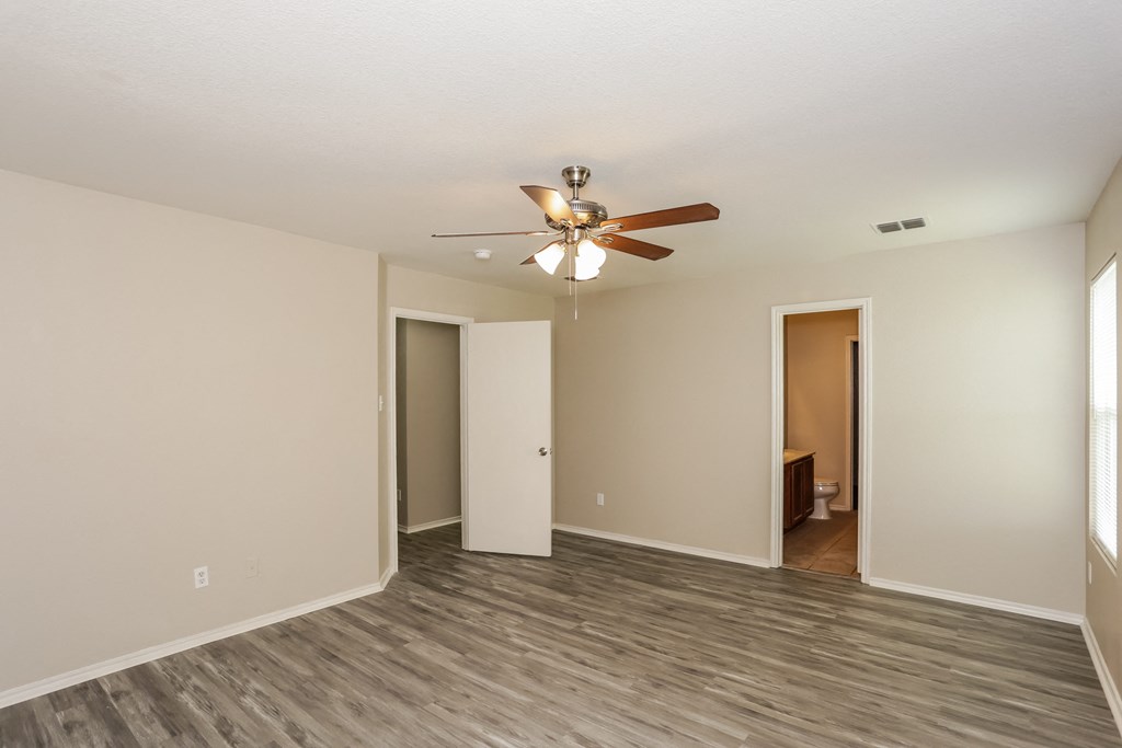 A room with a ceiling fan and light fixture, and a doorway leading to another room.