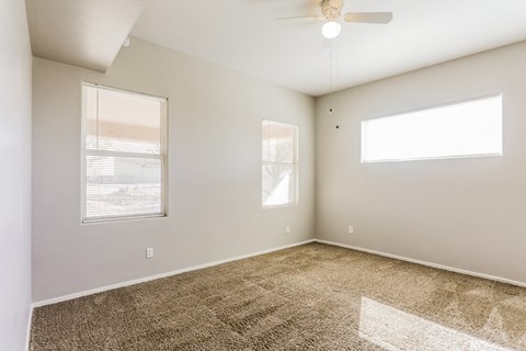 A room with a carpeted floor, a ceiling fan, and two windows.