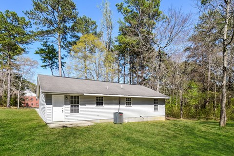 A small white house with a grey roof is surrounded by trees.