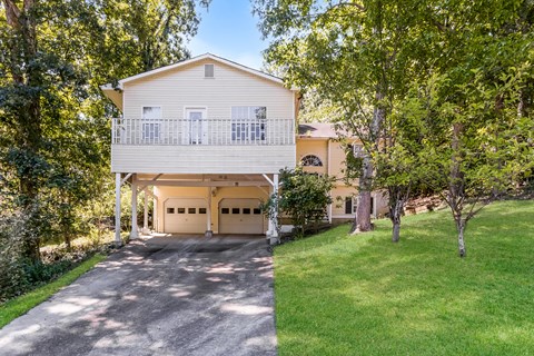 A house with a balcony and a garage is surrounded by trees.