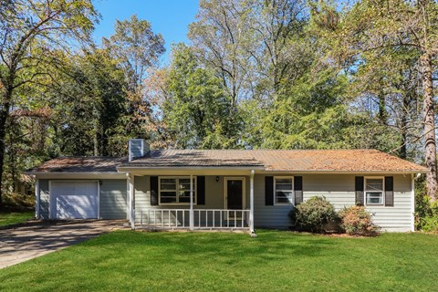 A house with a grey facade and a brown roof is surrounded by greenery.