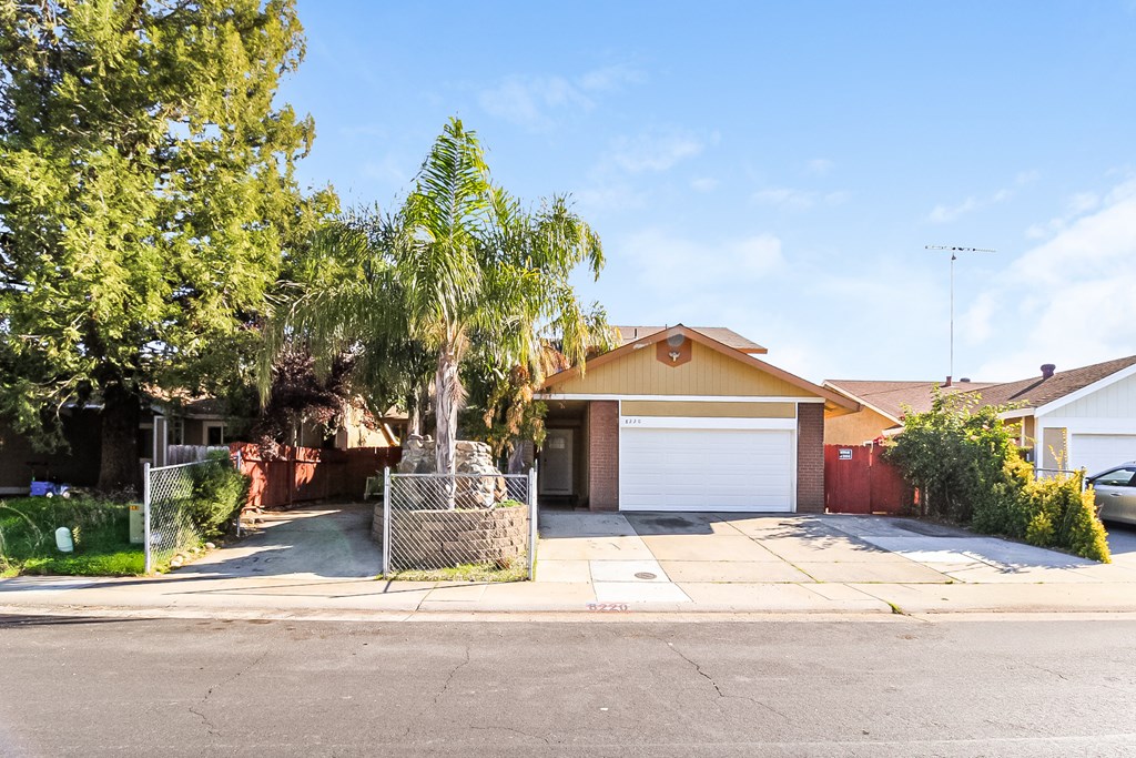 A house with a white garage door is surrounded by greenery and a clear sky.