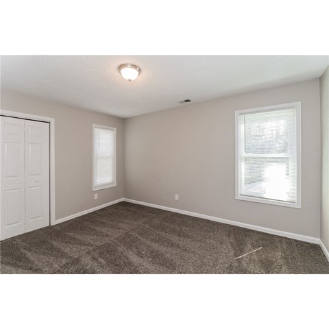 an empty bedroom with two windows and a door