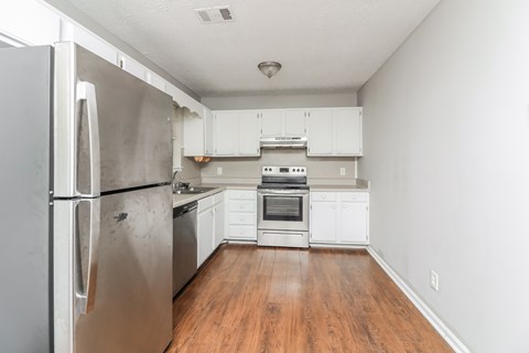 A kitchen with a refrigerator on the left and a stove top oven in the middle.