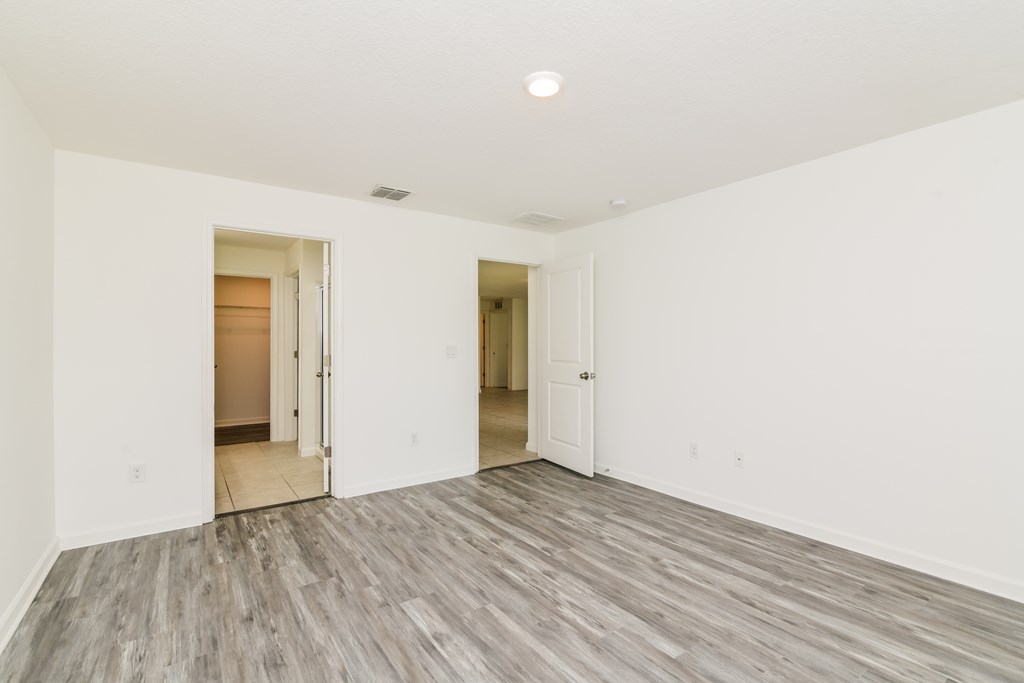 A room with white walls and wood flooring with two doors.