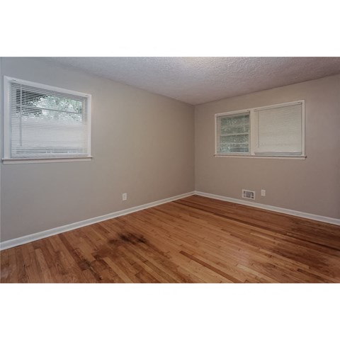 an empty bedroom with wood floors and two windows
