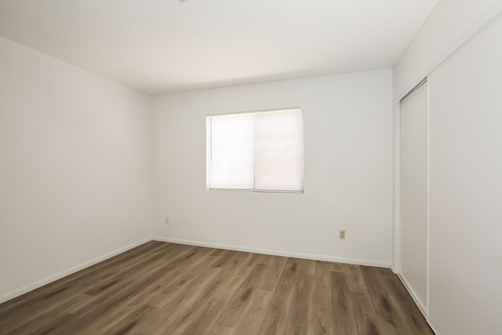A room with wooden flooring and a window with blinds.