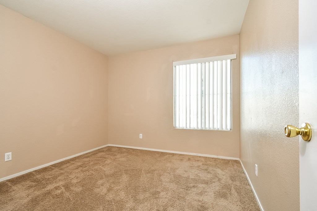 A room with a carpeted floor and a window with blinds.