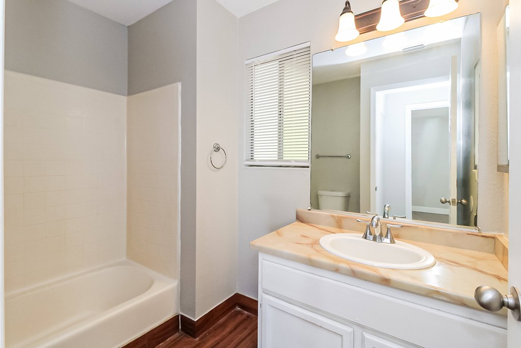 A white bathroom with a wooden vanity and a white bathtub.
