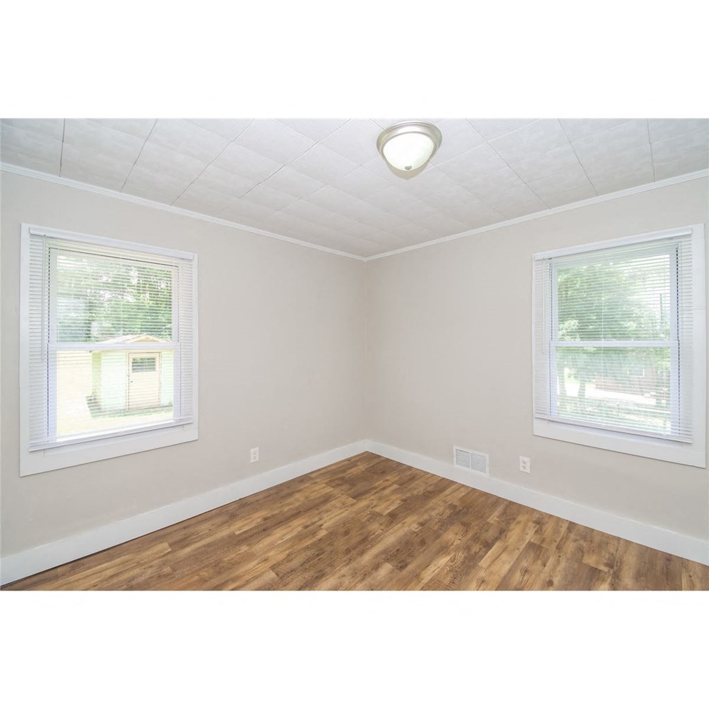 an empty room with a hard wood floor and two windows