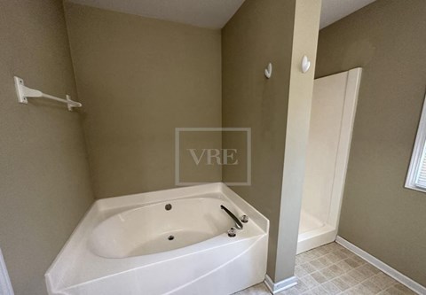 A white bathtub with a black faucet is in a bathroom with beige walls.