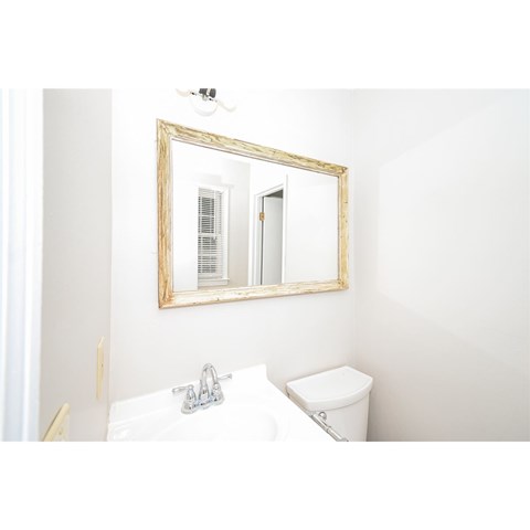 A bathroom with a toilet, sink, mirror, and light fixture.