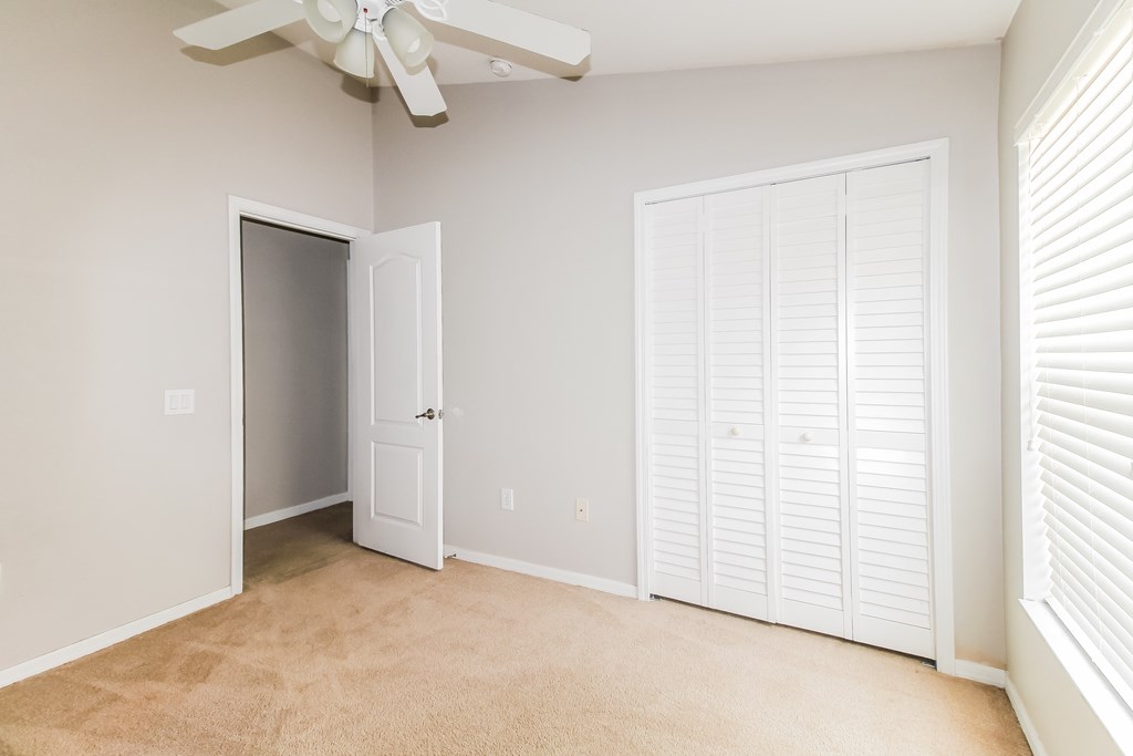 A room with a ceiling fan and white closet doors.
