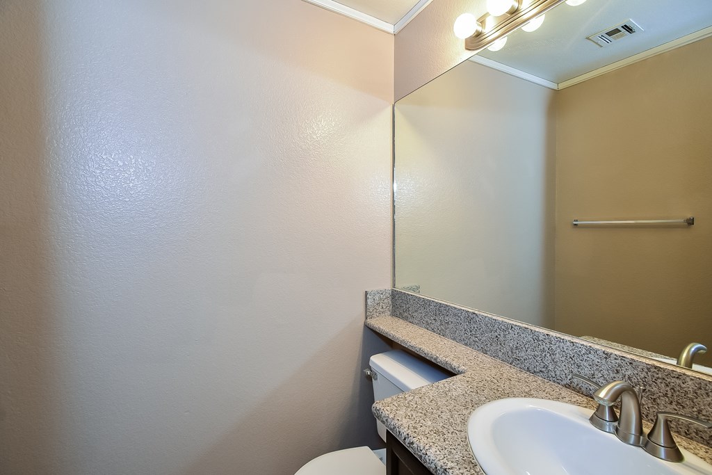 A bathroom with a toilet, sink, mirror and light fixture.