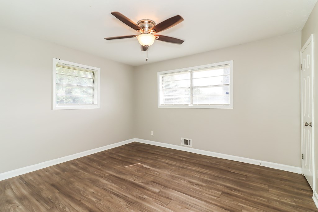 A room with a ceiling fan and two windows.
