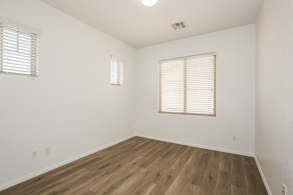 A room with wooden floors and two windows with blinds.
