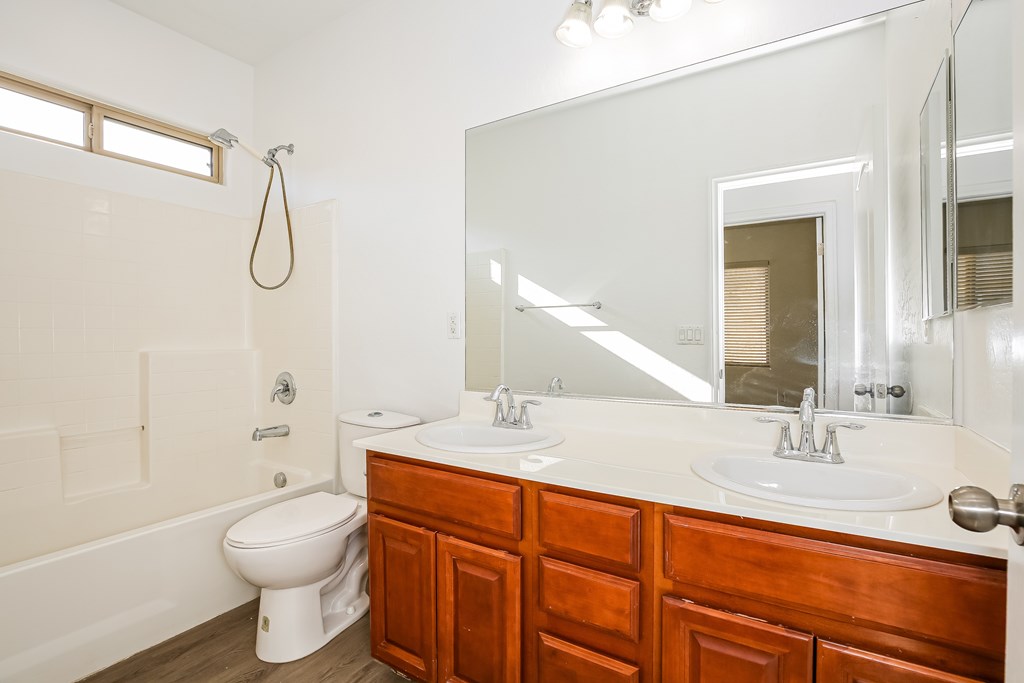 A white bathroom with a wooden vanity and a white toilet.