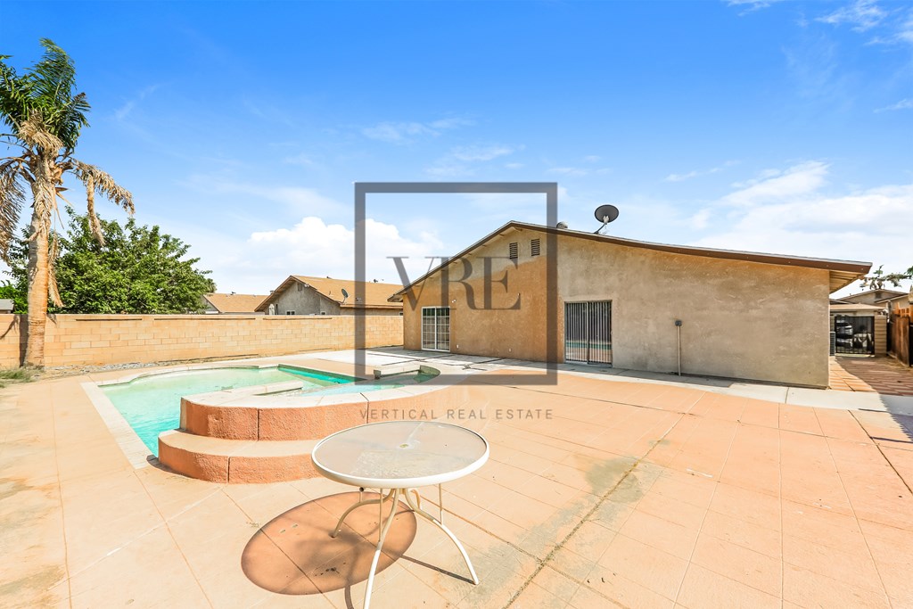 A pool with a table and chairs in front of a house.