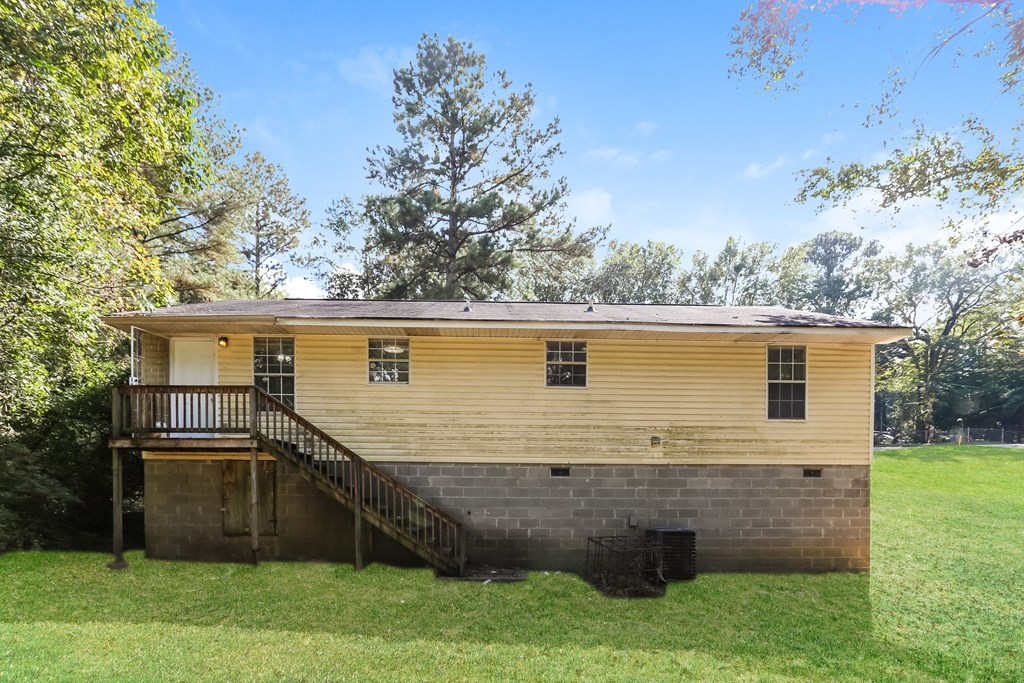 A yellow house with a porch and a tree in the background.