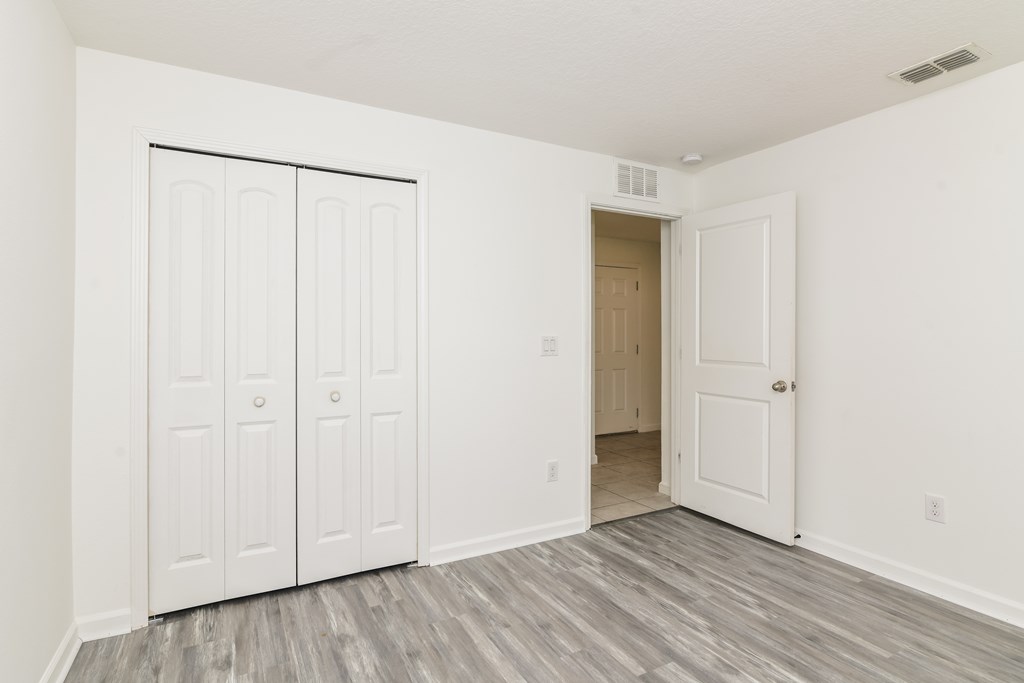 A room with white walls and a grey floor with a white door and a white wardrobe.