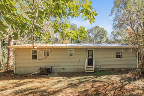 A house with a black door and a window is surrounded by trees.