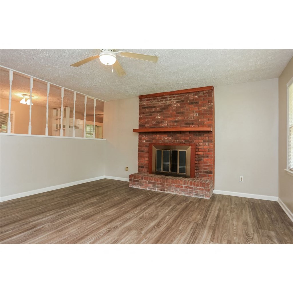 an empty living room with a brick fireplace and a ceiling fan