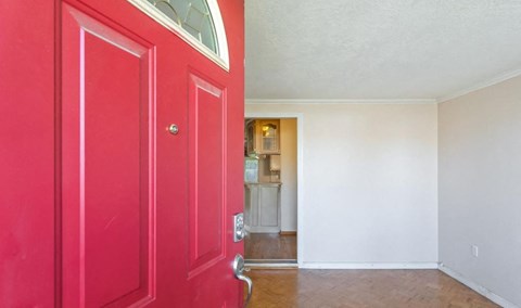 a red door in a room with a kitchen in the background