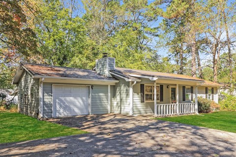 A house with a grey garage door and a white door is surrounded by trees.