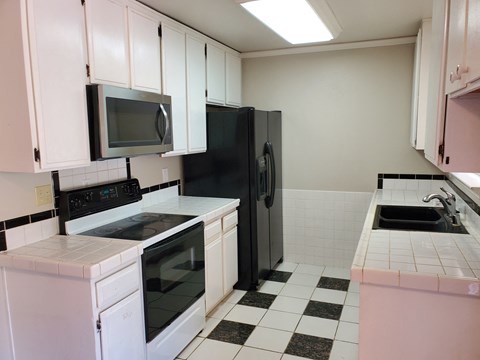 A black refrigerator is in a kitchen with white cabinets.