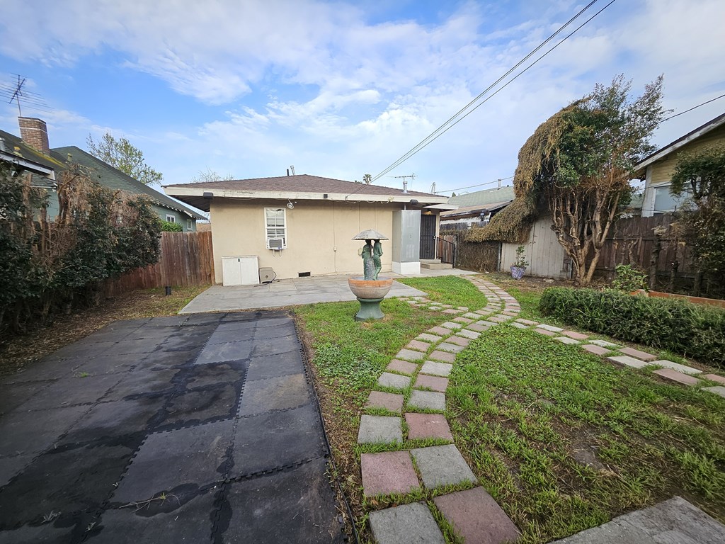 A backyard with a paved walkway and a brick pathway leading to a house.