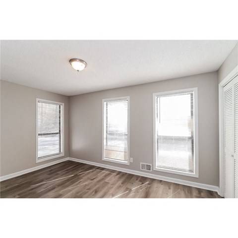 an empty living room with three windows and wood flooring