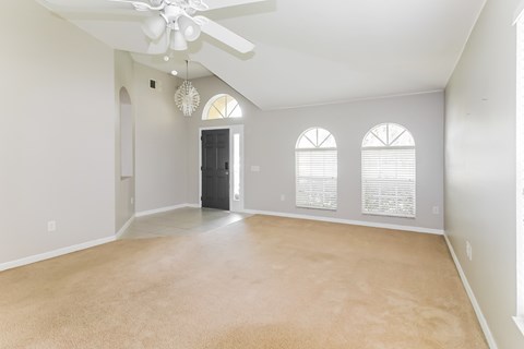 A spacious room with a ceiling fan and three windows.