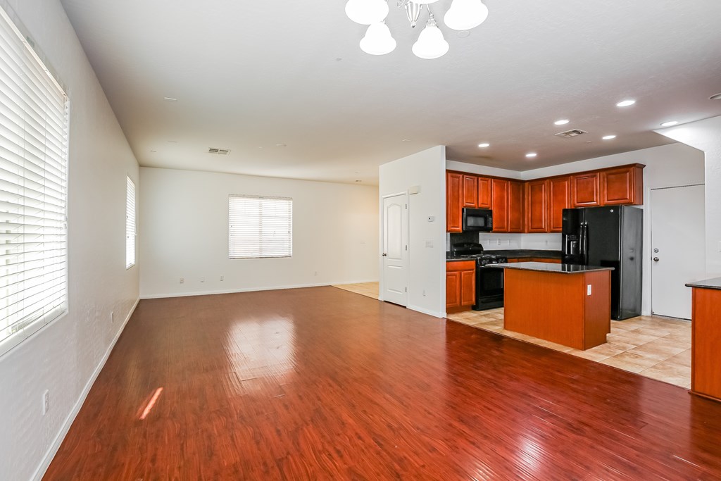 A spacious living room with wooden floors and a kitchen area in the background.