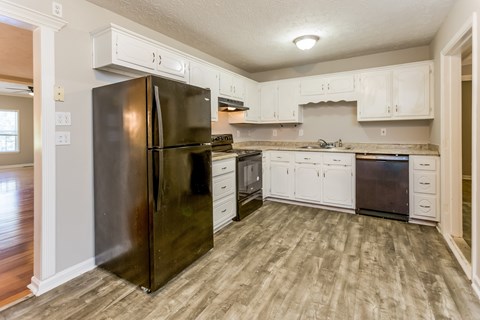 A black refrigerator in a kitchen with white cabinets.