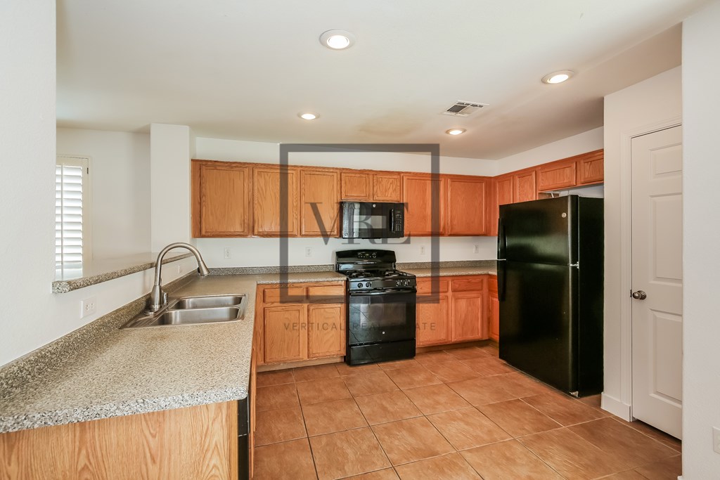 A kitchen with a black fridge and a black trash can.