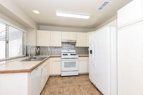 A white kitchen with a refrigerator, sink, and stove.