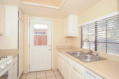 A kitchen with a white door and a window with blinds.