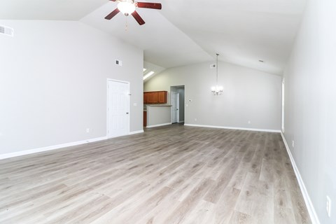 A room with a ceiling fan and light, hardwood floors, and a doorway leading to another room.