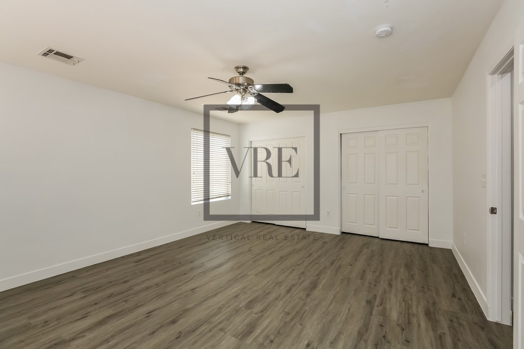 A room with a ceiling fan and a large window with blinds.