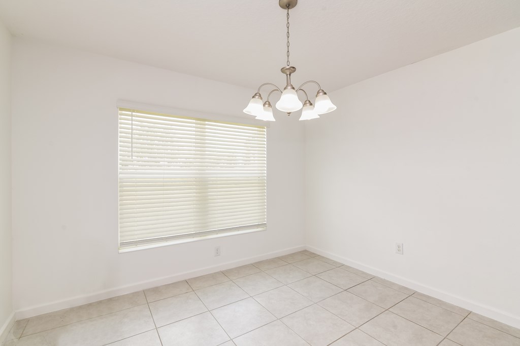A room with a window covered by blinds and a chandelier hanging from the ceiling.