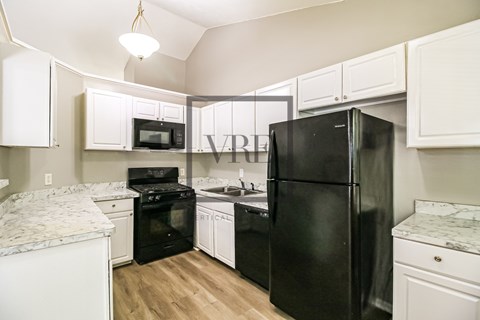 A black refrigerator is in a kitchen with white cabinets.