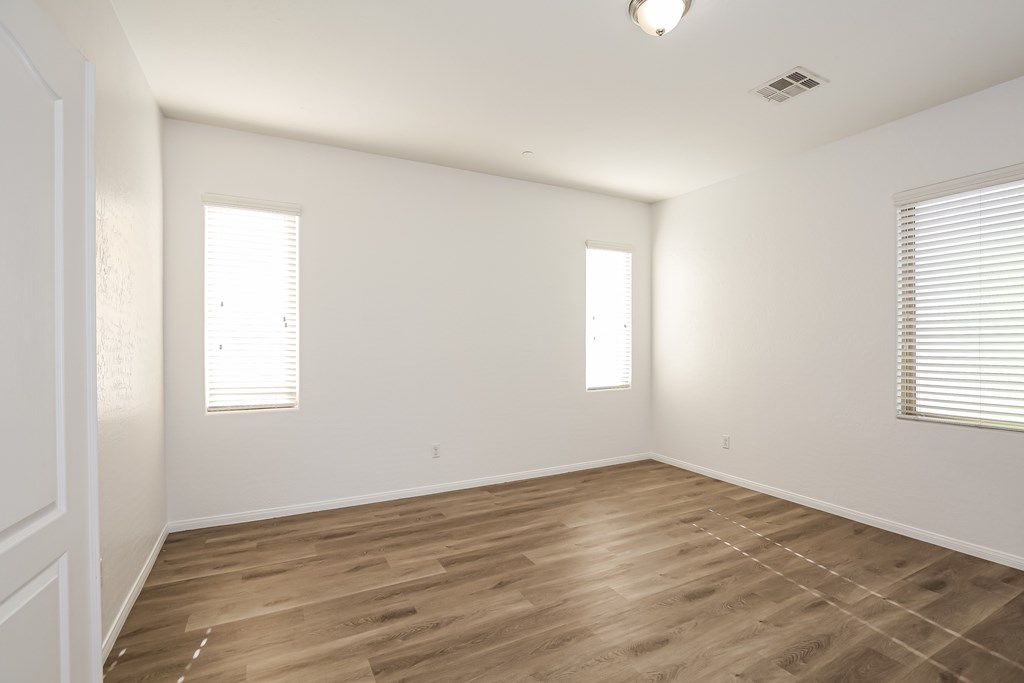 A room with wooden flooring and two windows.
