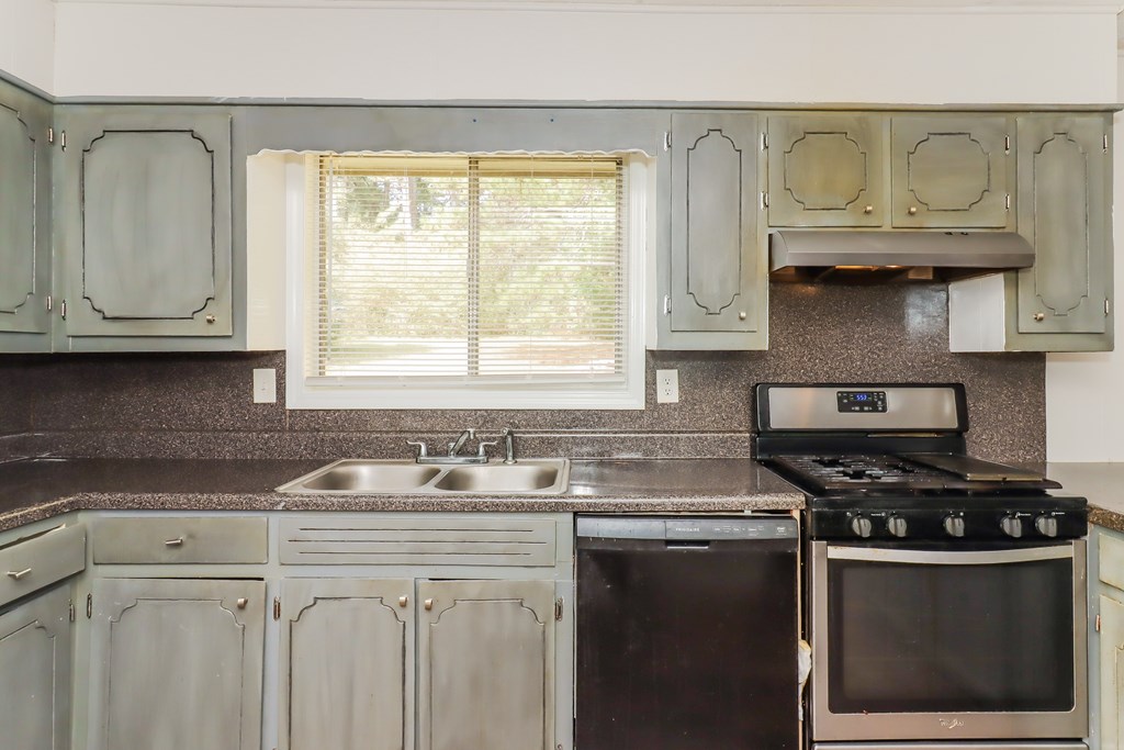 A kitchen with a stove, sink, and cabinets.